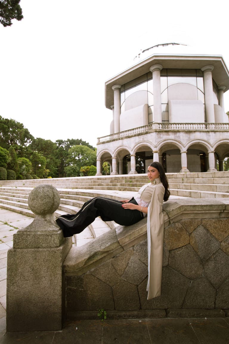 II Acto look reclining on a stone balustrade, with a long cream sash.
