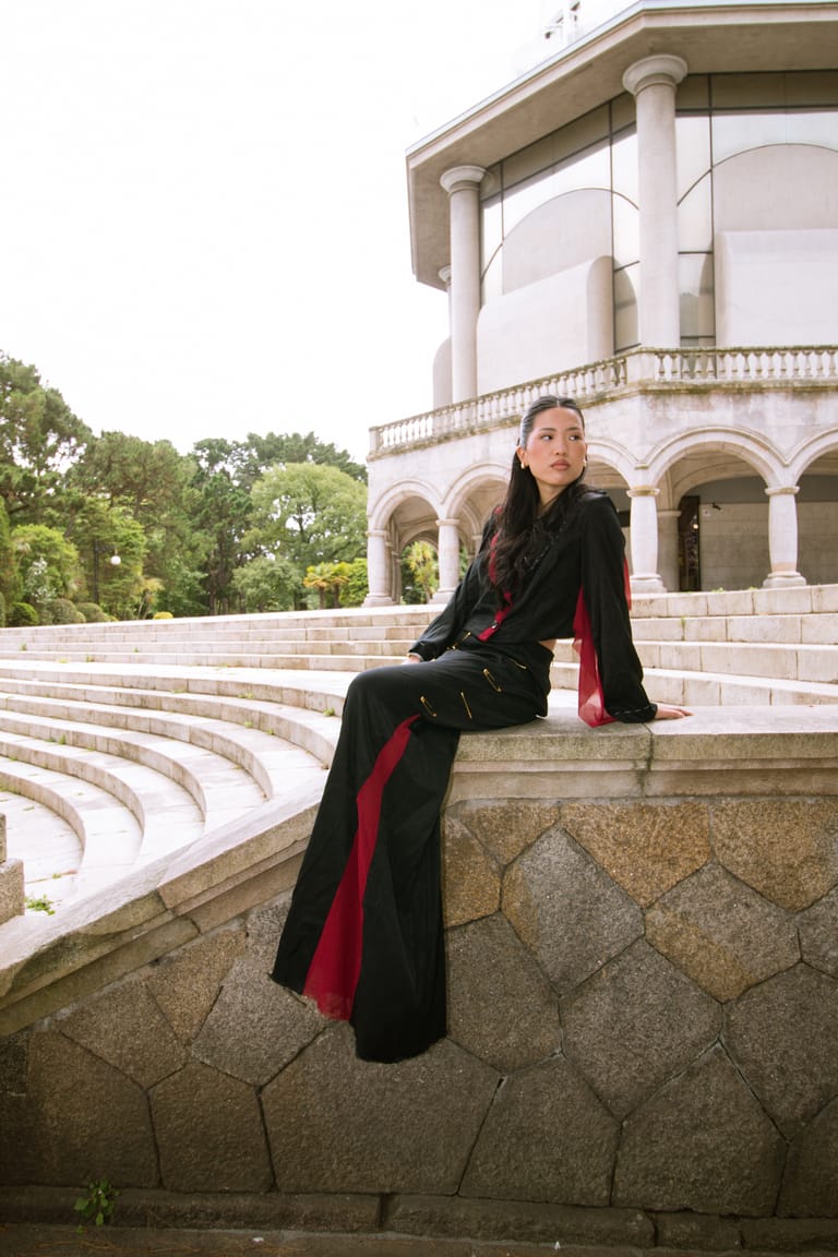II Acto look seated on the low wall, black with a red side panel, the pavilion arcade behind.