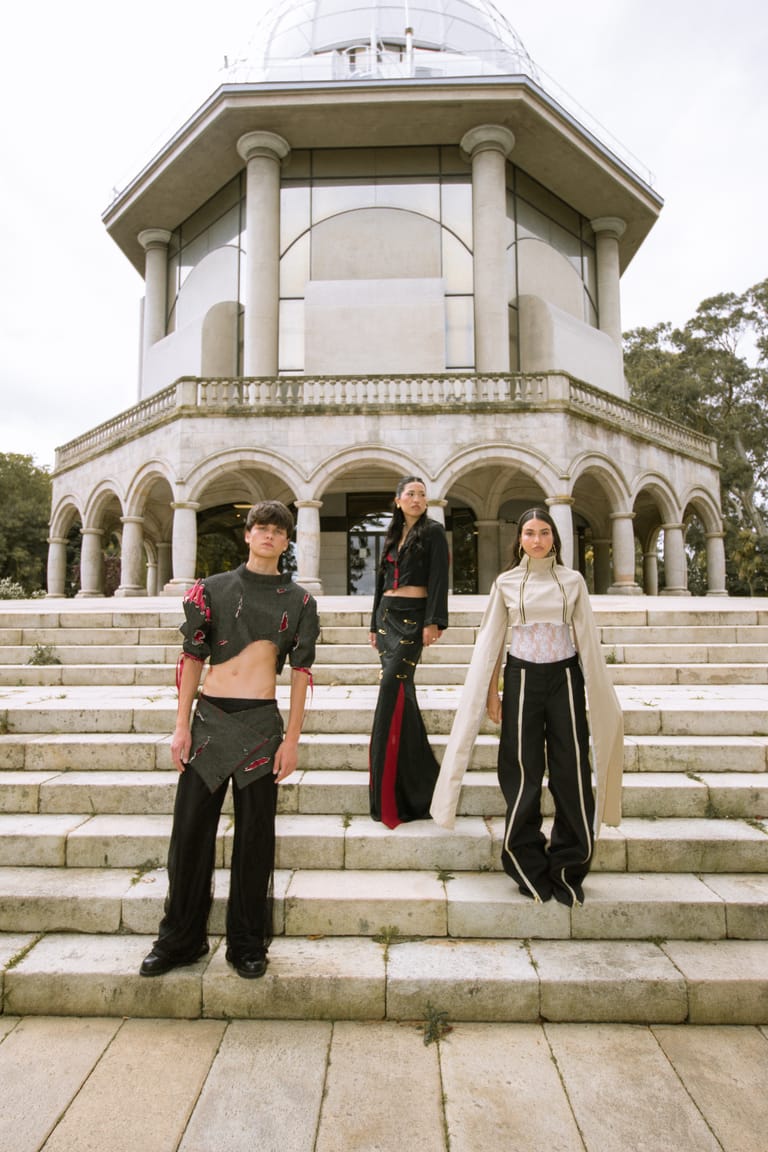 Three II Acto looks on the steps of the domed neoclassical pavilion: a cropped dark top with layered skirt, a black bodice with red-panelled trousers, and a cream cropped jacket with long draped sleeves.