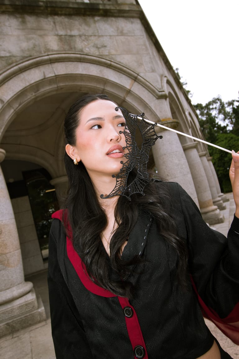 Close portrait of an II Acto look with a black lace hairpiece and a red-trimmed jacket.