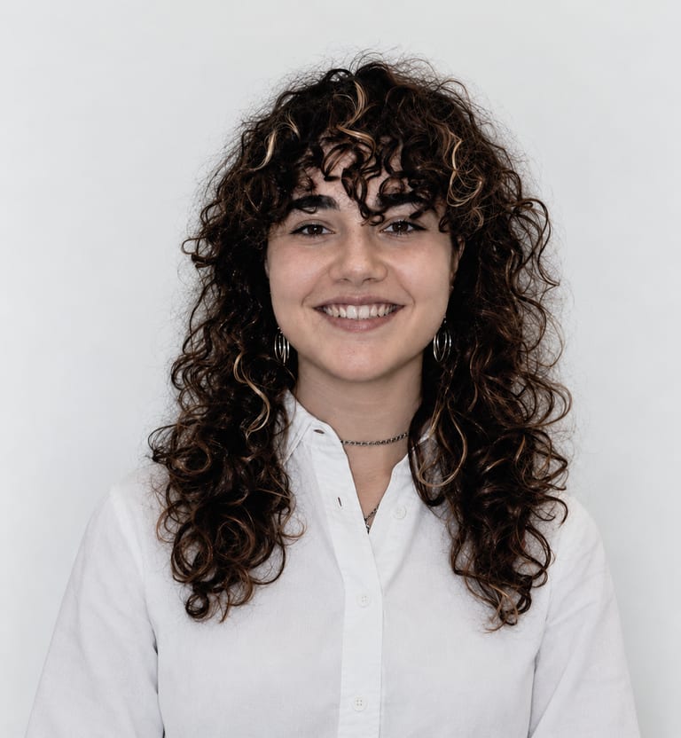 Portrait of Laura Naroa, smiling, wearing a white shirt against a light background.